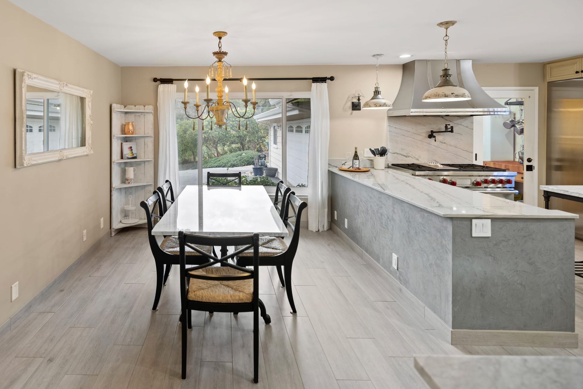 A dining room with a long table and chairs and a kitchen.