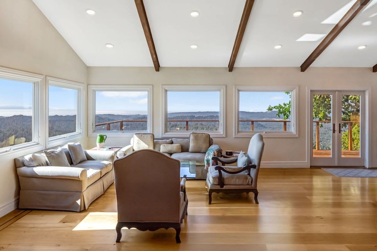 Spacious living room with light wood floor, large windows, and mountain views.