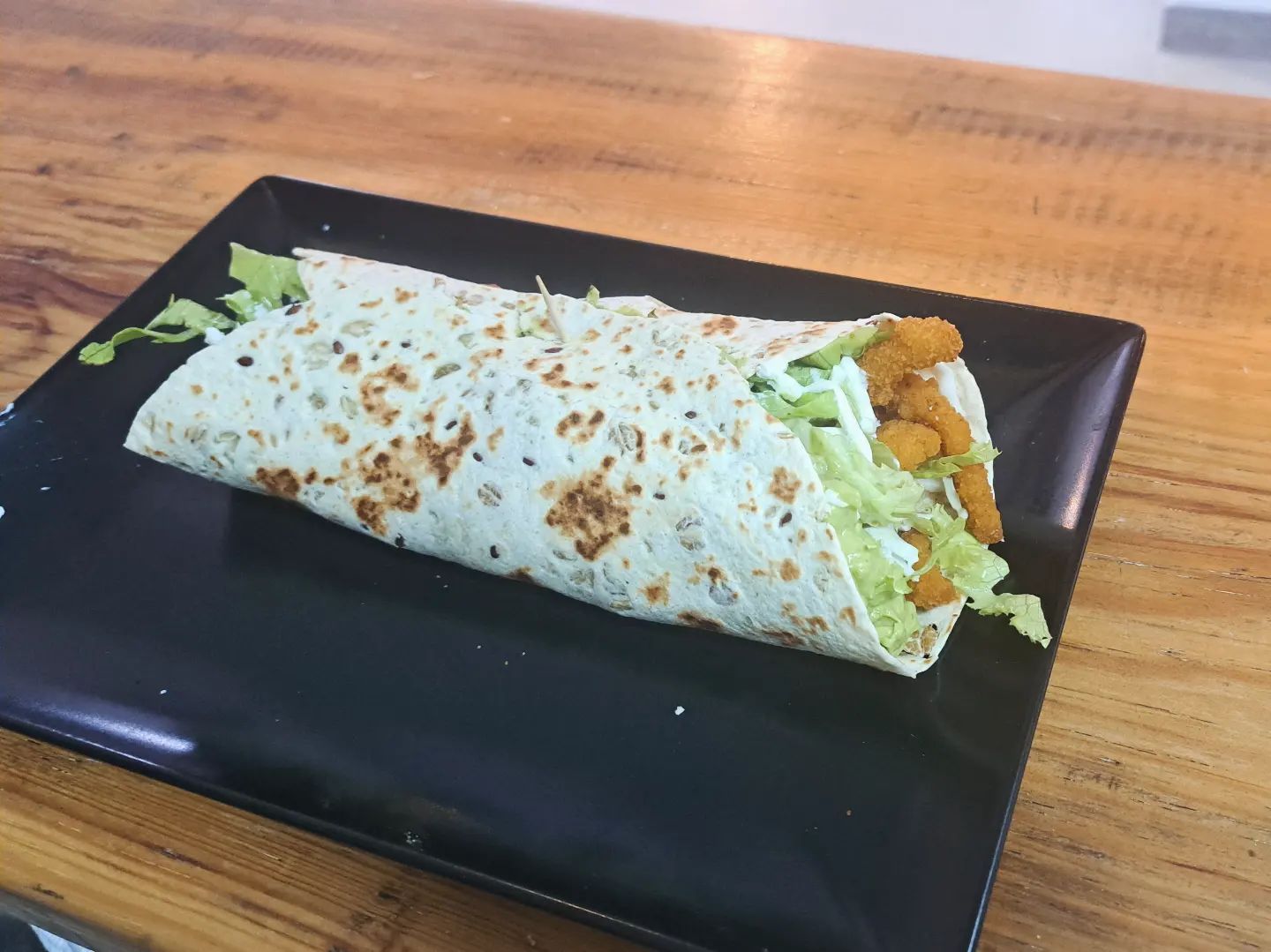 Una tortilla con lechuga y pollo en un plato negro sobre una mesa de madera.