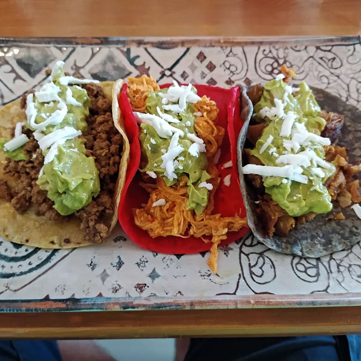 Tres tacos con guacamole y queso en un plato sobre una mesa.