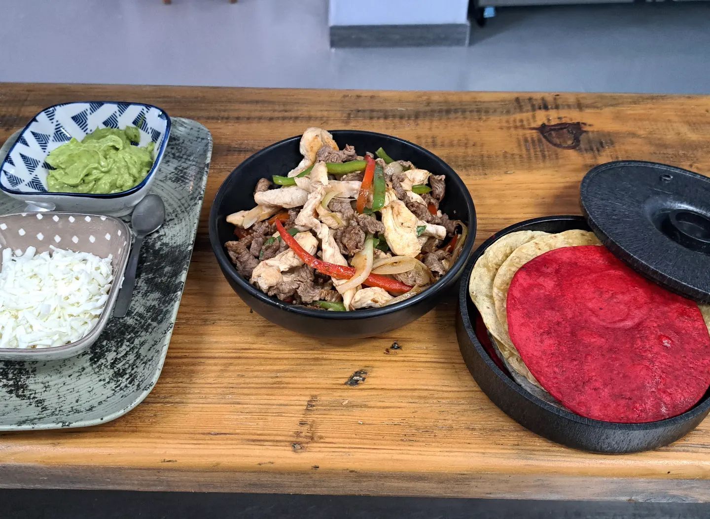 Una mesa de madera cubierta con tazones de comida, tortillas, guacamole y arroz.