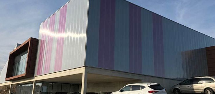 Dos coches están aparcados delante de un gran edificio con una fachada de rayas rosas y moradas.
