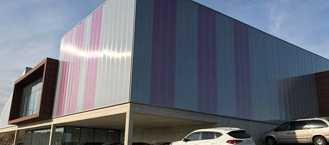 Dos coches están aparcados delante de un gran edificio con una fachada de rayas rosas y moradas.