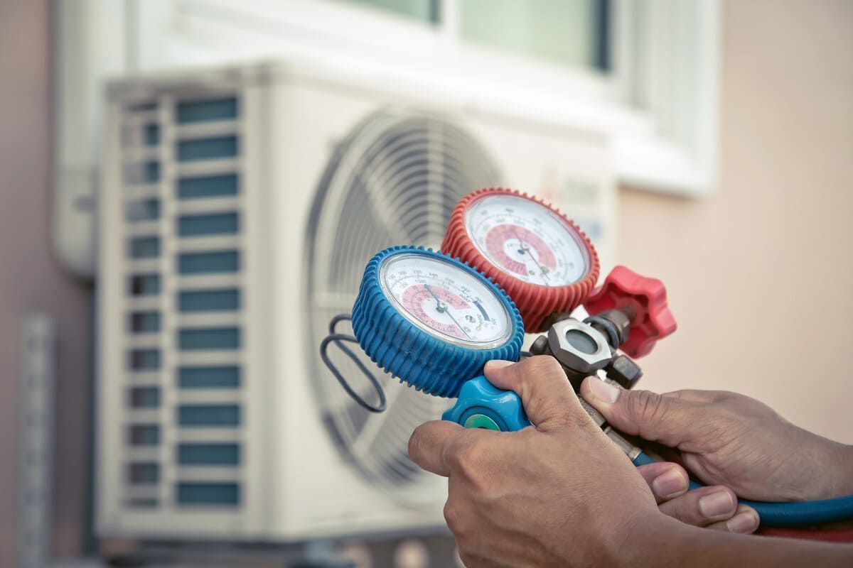 Una persona sostiene un par de medidores frente a un acondicionador de aire.