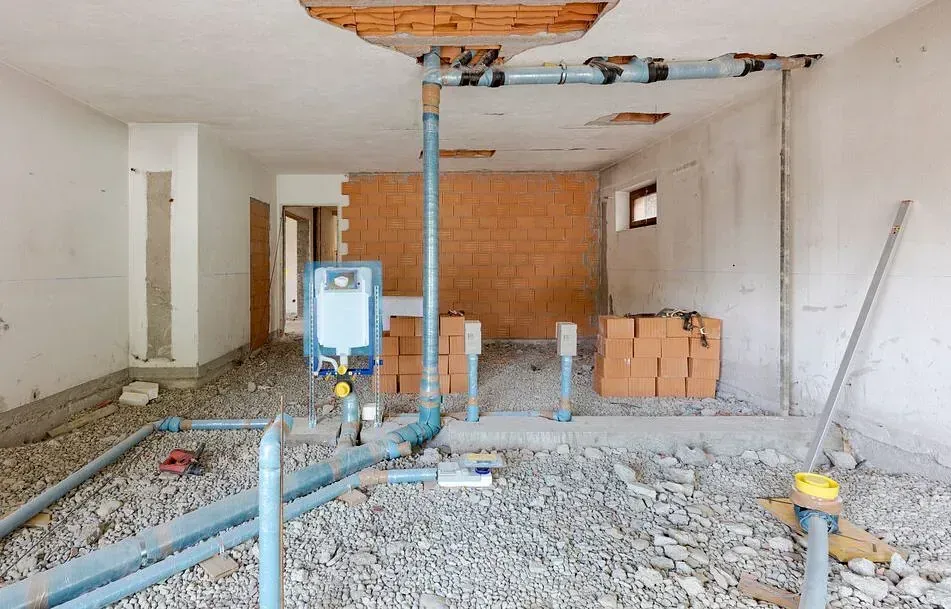 Una habitación en construcción con tuberías y ladrillos en el suelo.