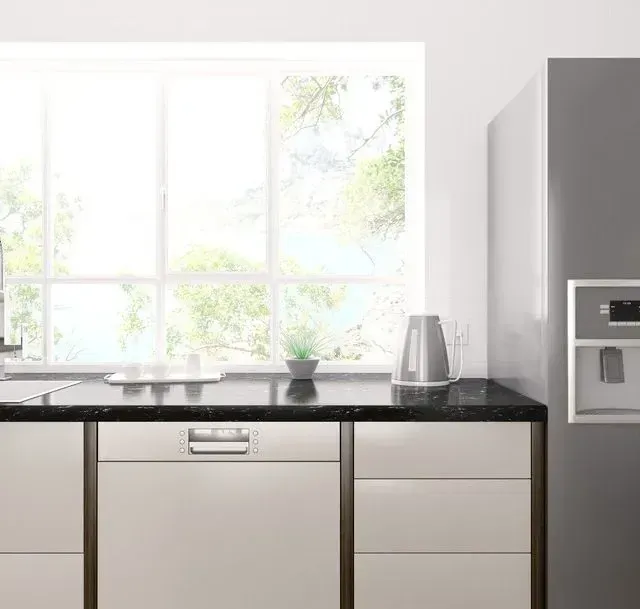 Una cocina con gabinetes blancos, un refrigerador, un lavavajillas y una ventana.