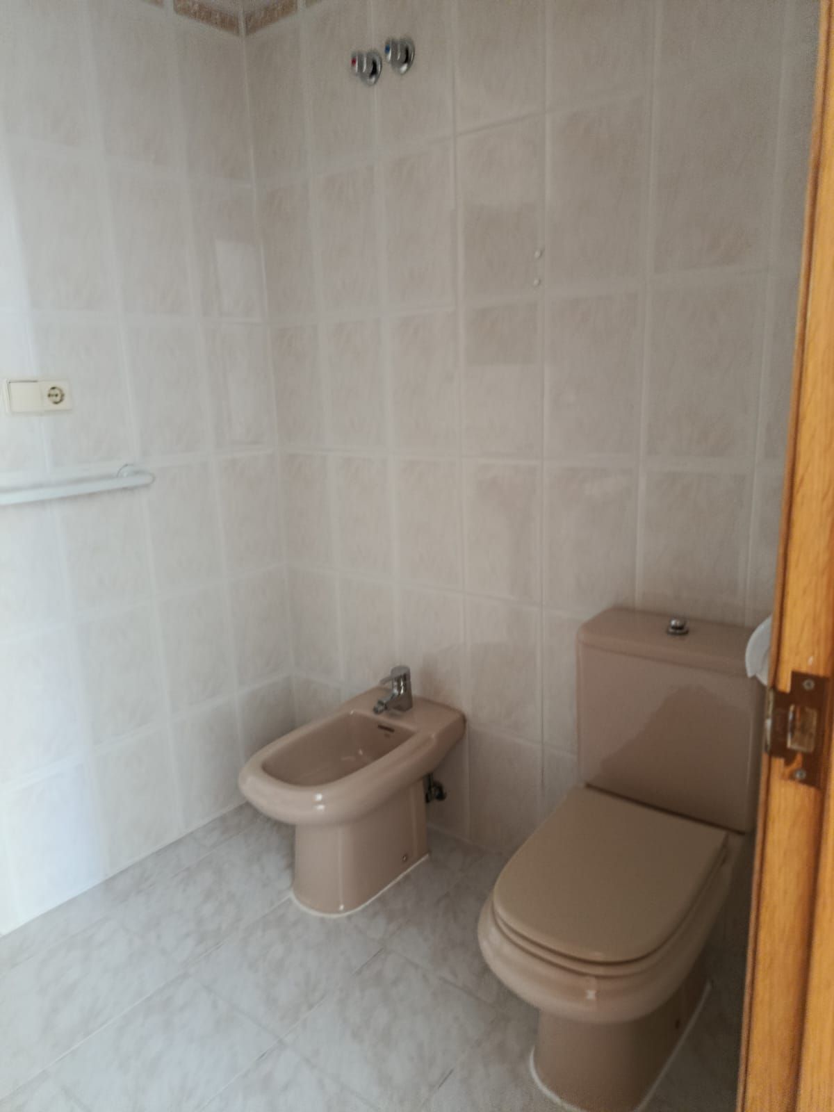 Baño pequeño con azulejos, con un inodoro y un bidé junto a una barra de apoyo.