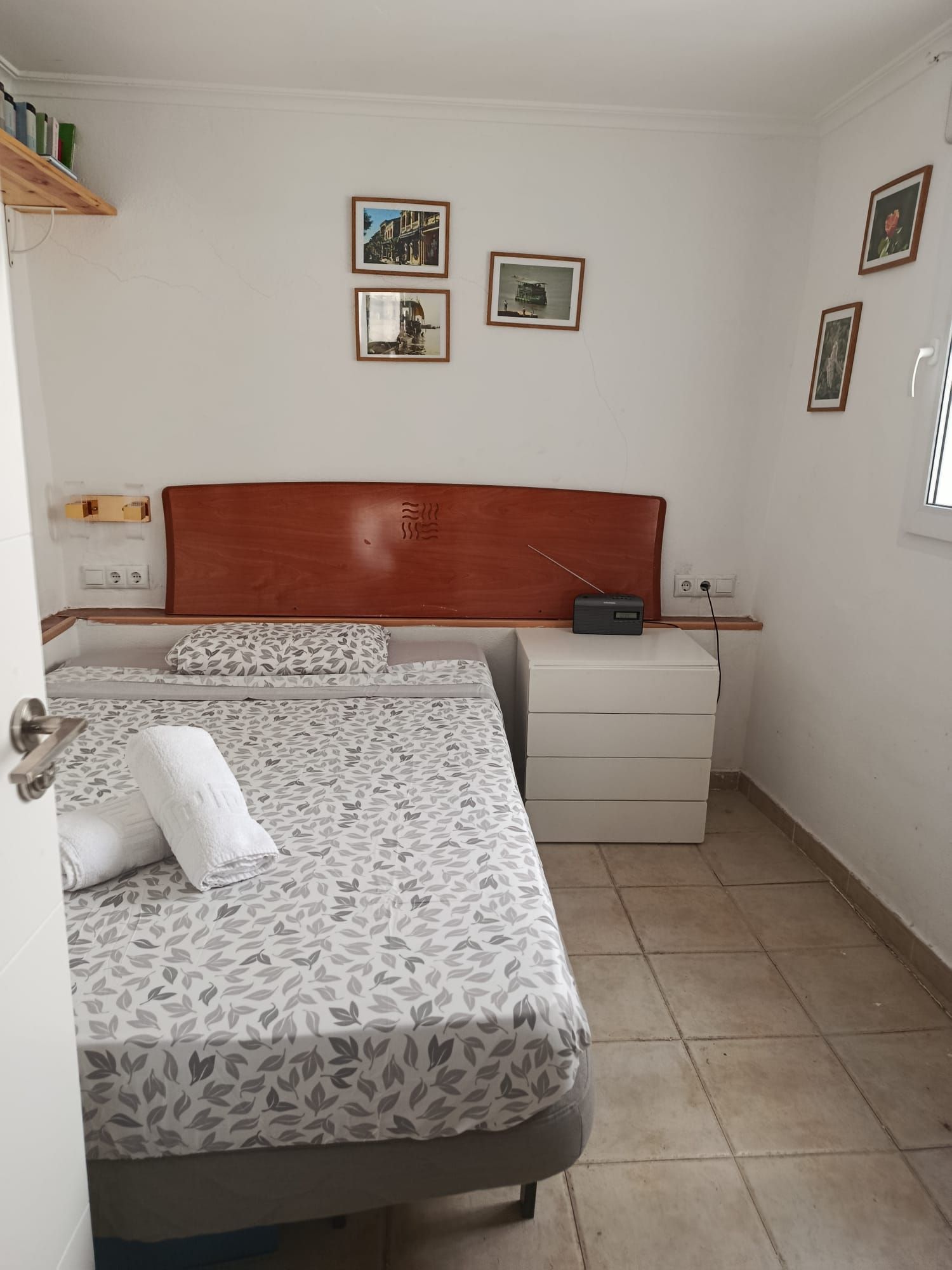Dormitorio pequeño con dos camas, suelo de baldosas, paredes blancas y cuadros enmarcados sobre un cabecero de madera.