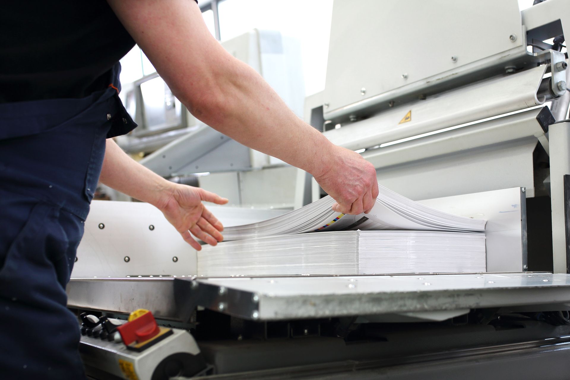 Homme mettant des papiers en forme sur une machine à imprimerie.