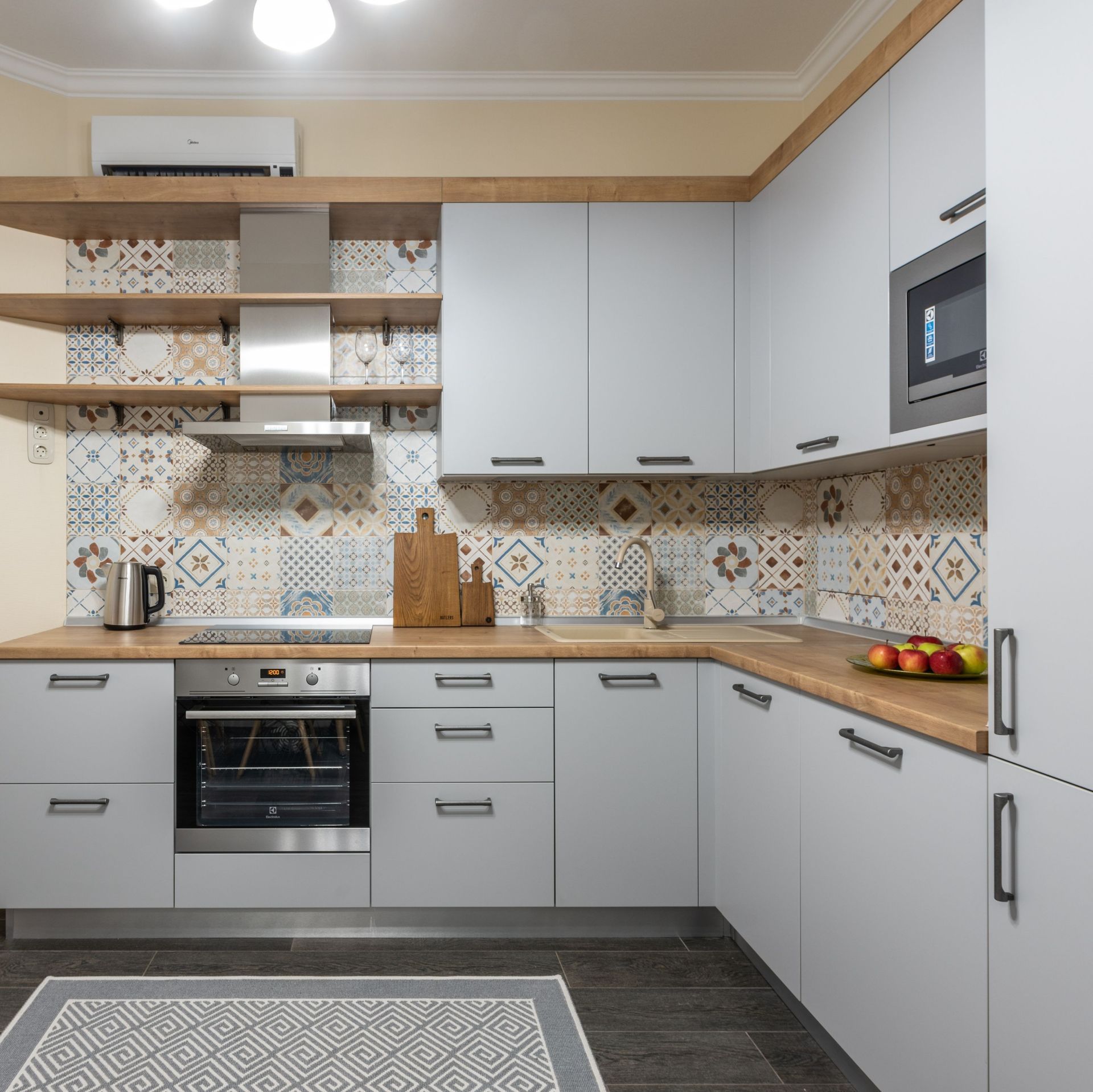 Cocina moderna en forma de L de color gris con salpicadero estampado, horno empotrado y encimeras de madera.