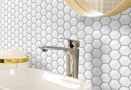 Grifo de baño cromado y lavabo blanco sobre un salpicadero de azulejos hexagonales blancos.