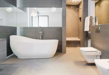 Baño moderno con bañera independiente, ducha de cristal e inodoro en tonos neutros.