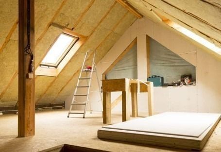 Dormitorio abuhardillado en proceso de renovación con escalera, tragaluz, vigas a la vista y una plataforma de cama parcialmente construida.