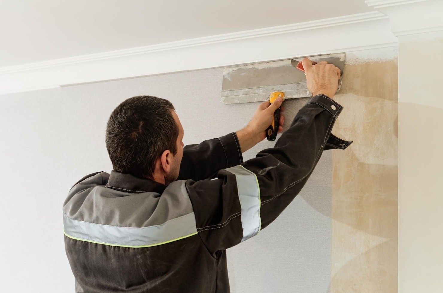 Un trabajador utiliza una espátula para reparar una grieta cerca del techo en una pared interior.