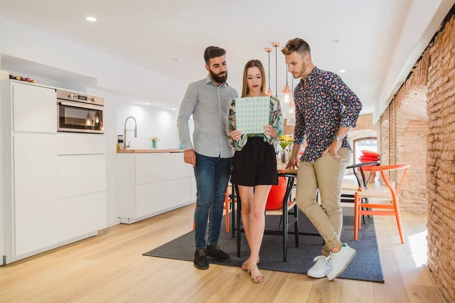 Tres personas prueban una tableta en una cocina moderna y luminosa; una de ellas está descalza sobre una alfombra.
