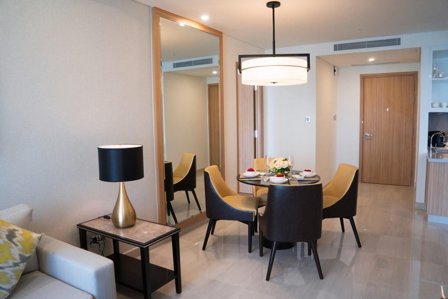 Comedor moderno con mesa redonda, sillas negras, espejo y lámpara en un apartamento luminoso.