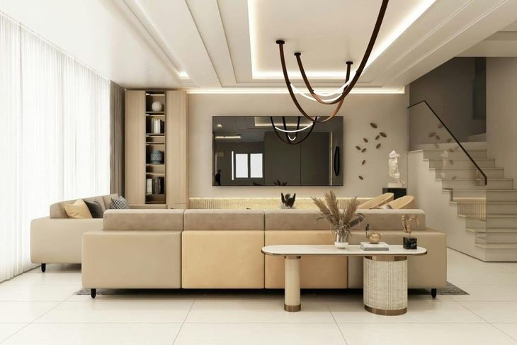 Sala de estar moderna de color beige con sofá modular, mesa de centro, lámpara de araña y escalera al fondo.