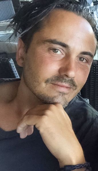 Mann mit dunklem Haar und Schnurrbart, stützt das Kinn auf die Hand und blickt in die Kamera.