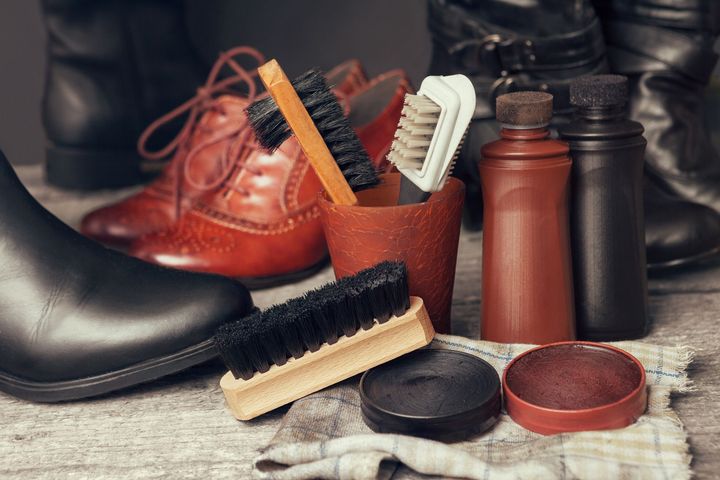Des brosses et du cirage entourés de chaussures.