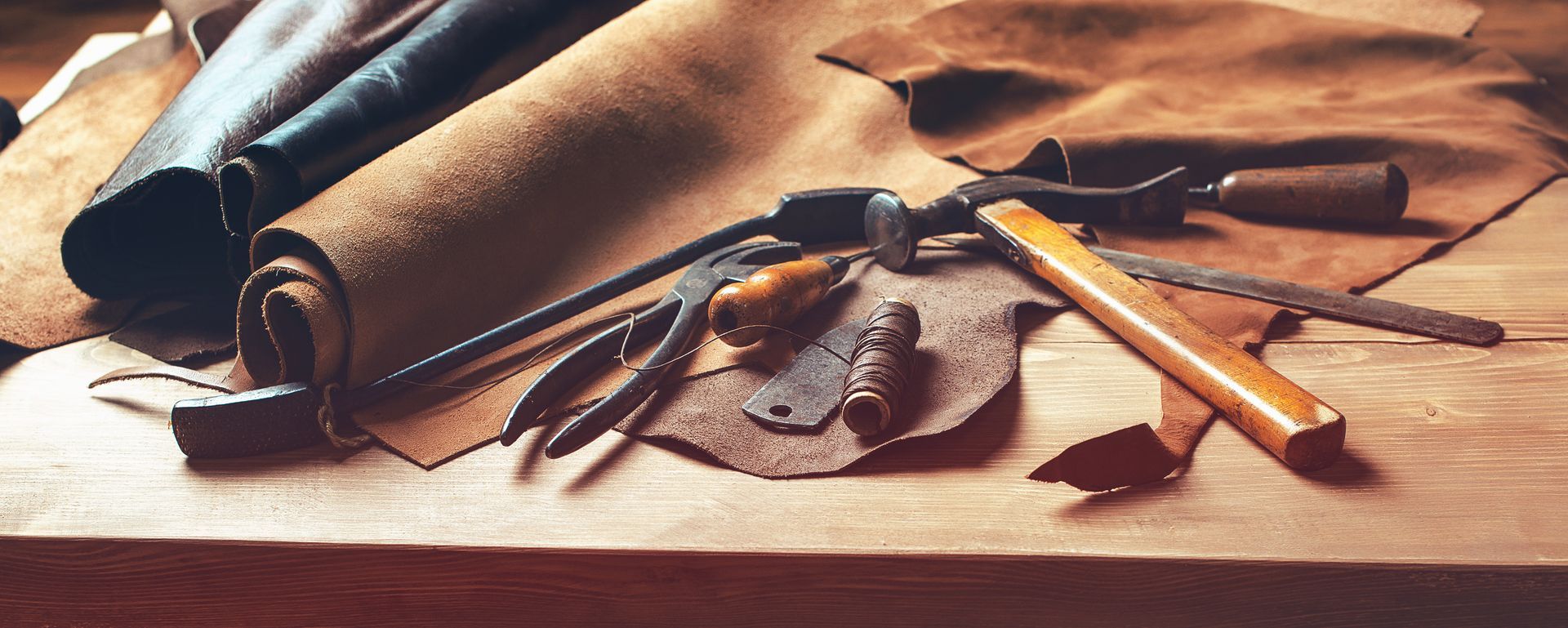 Des outils de cordonnerie et de la peau de cuir posés sur un établis.