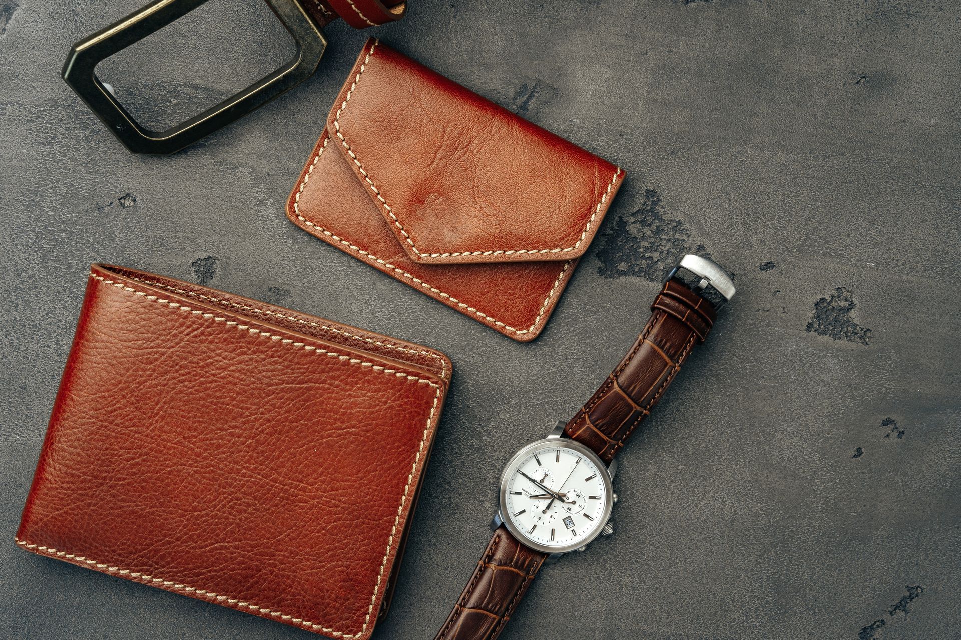 Un porte-monnaie, la boucle d'une ceinture un portefeuille et une montre posés sur une surface.