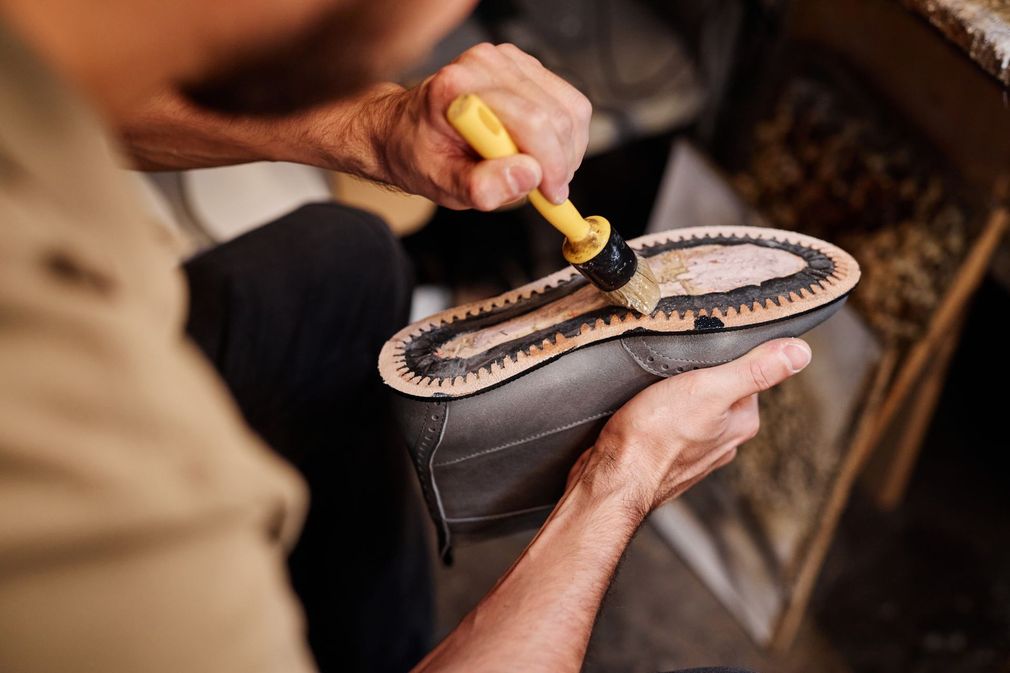 Un cordonnier qui applique de la colle sur la semelle d'une chaussure.