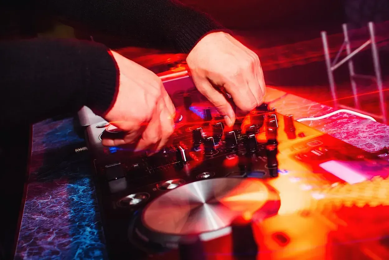 DJ en el trabajo: manos sobre una mesa de sonido con un plato giratorio plateado, luces de escenario que proyectan tonos rojos y azules.