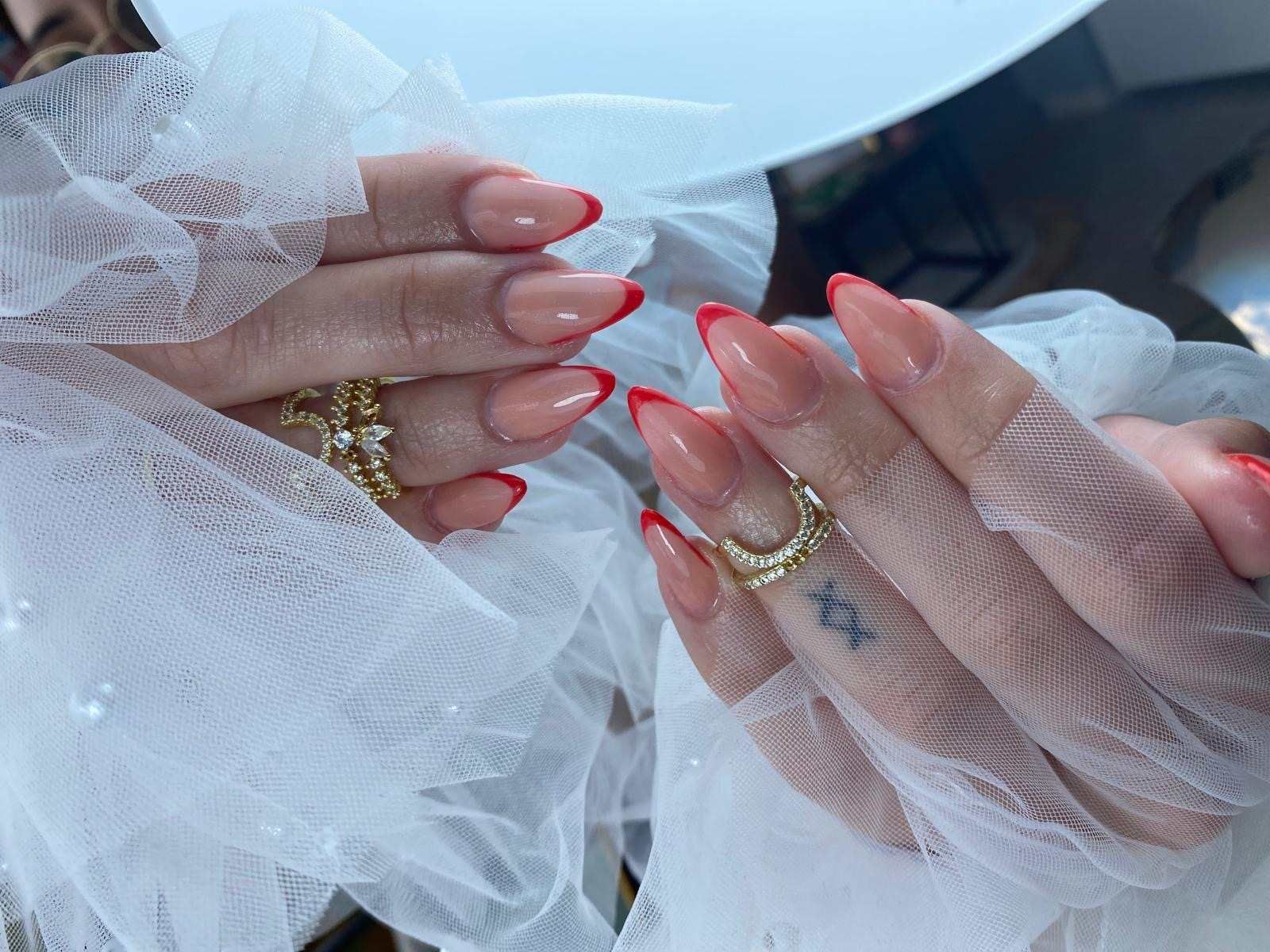 Un primer plano de las manos de una mujer con uñas rojas y un tatuaje en el dedo.