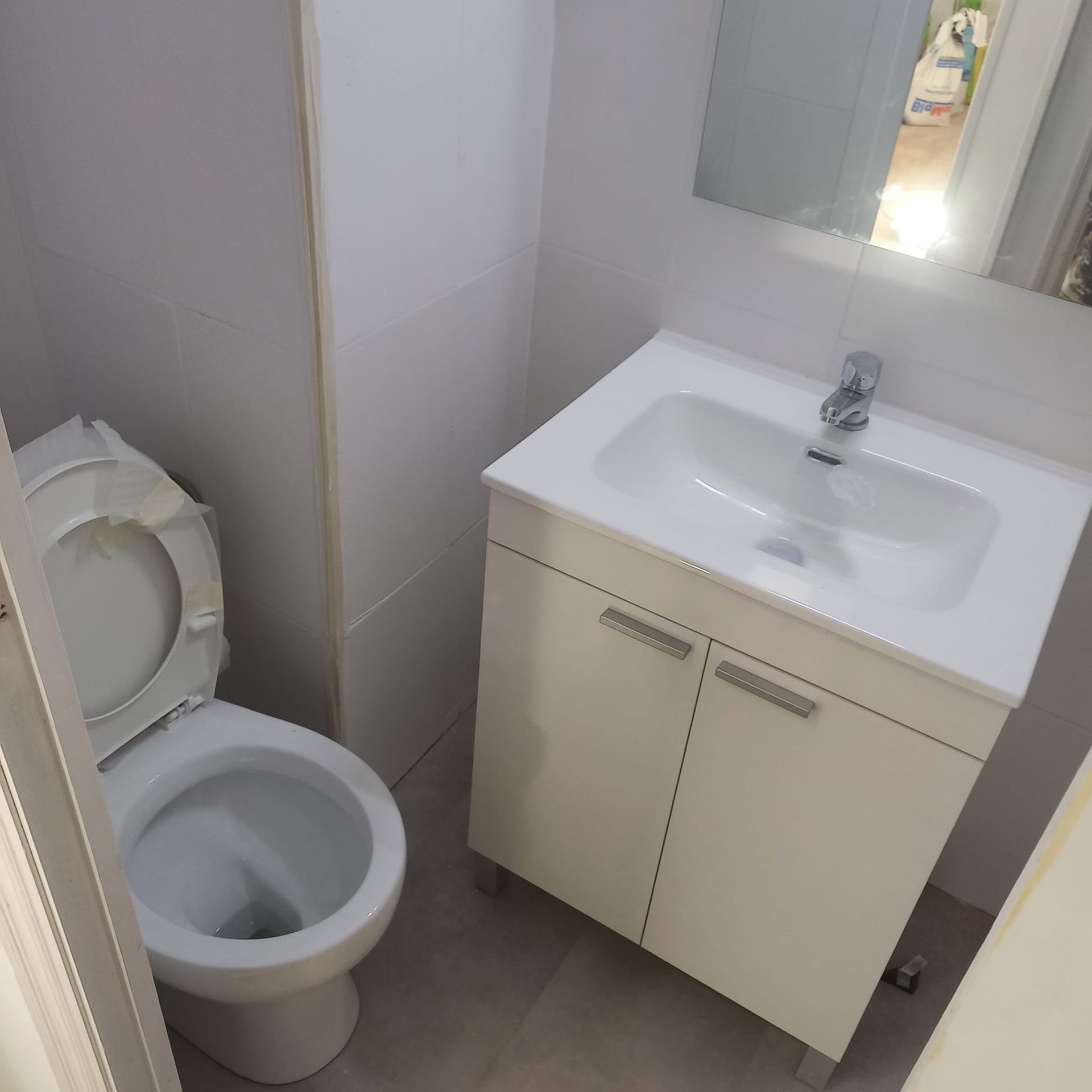 Un baño pequeño y luminoso con un inodoro blanco y un lavabo blanco a juego con grifo, visto desde una puerta.