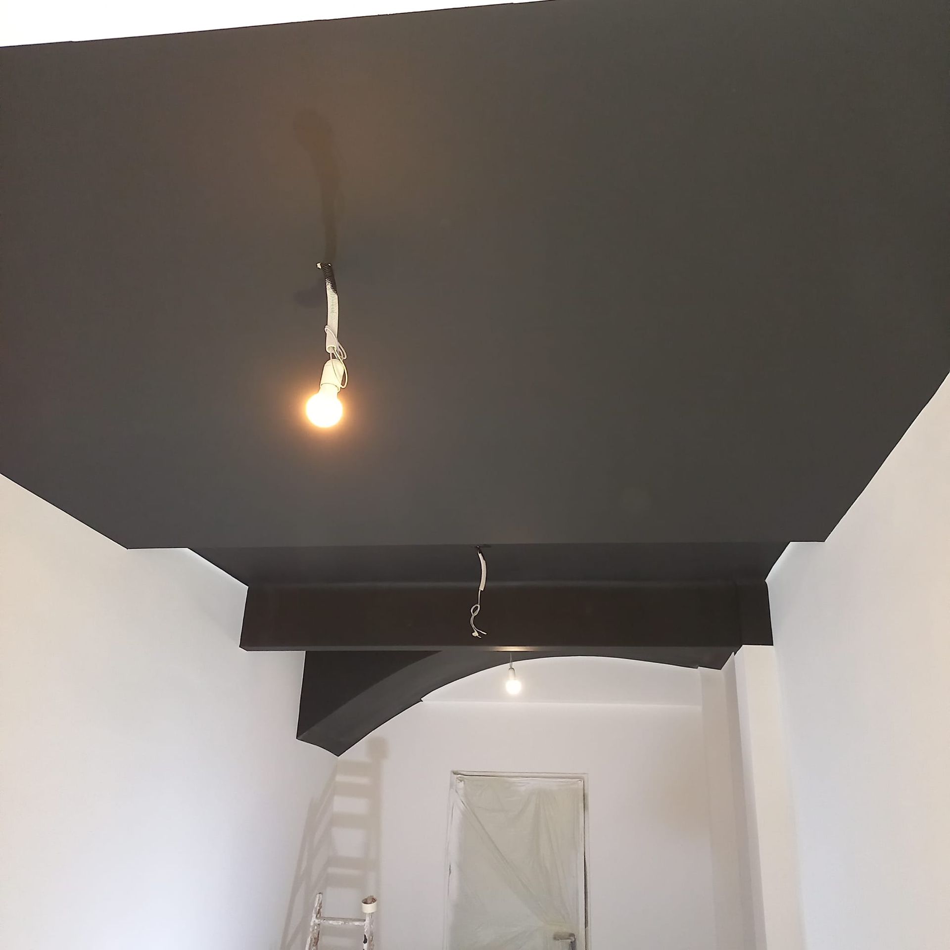 Una habitación reformada con un falso techo gris oscuro y una viga de soporte a la vista