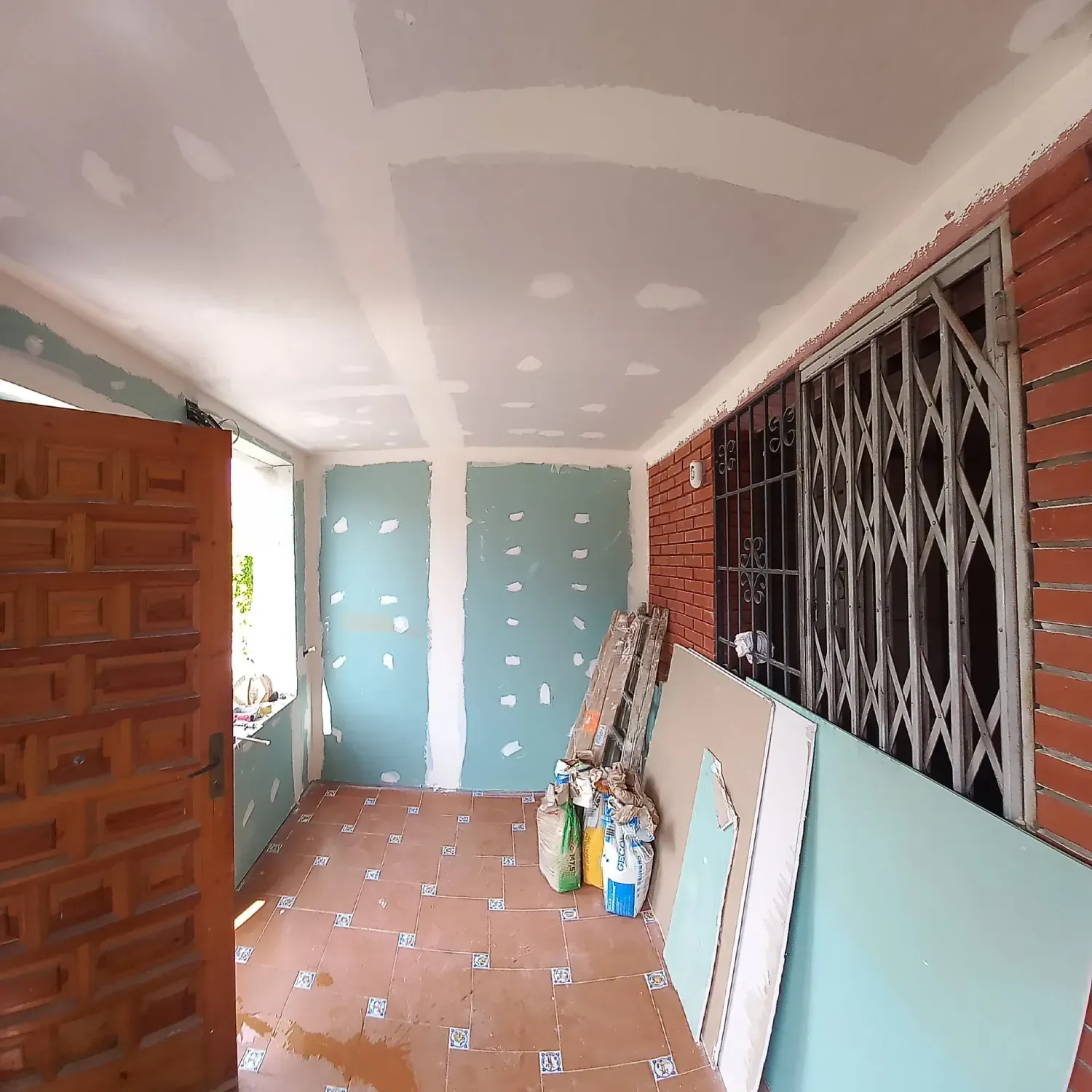 Un porche interior en proceso de renovación con paredes y techo de pladur sin terminar, revestimiento de ladrillo