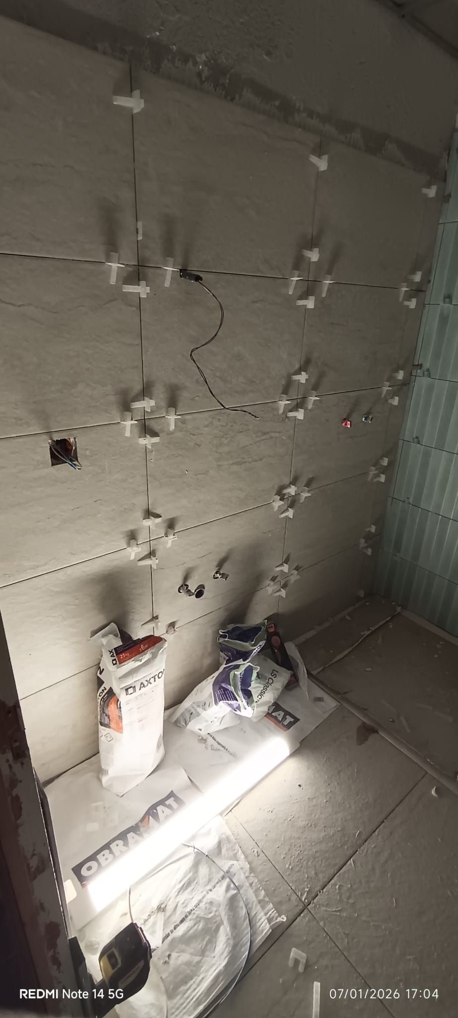 Una obra en construcción que muestra una pared preparada con clips de nivelación para azulejos