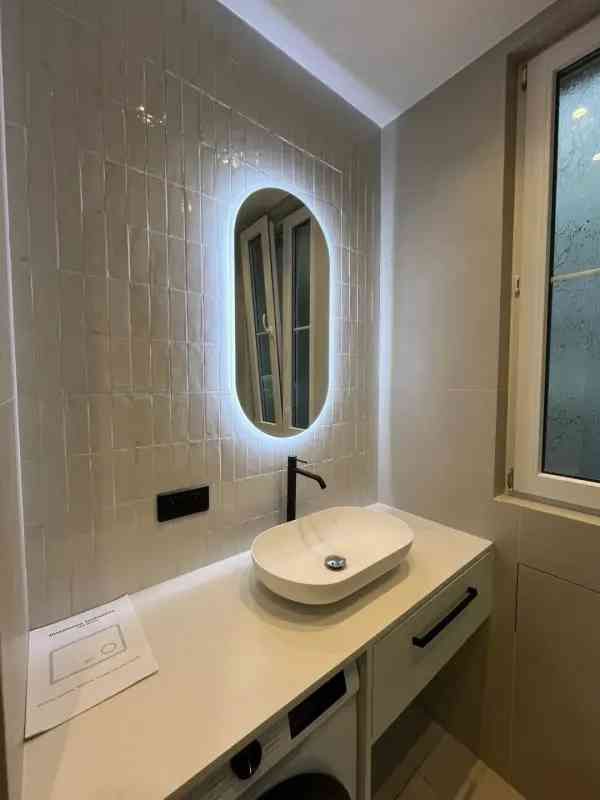 Un moderno mueble de baño con lavabo blanco sobre encimera, grifo negro mate y espejo ovalado