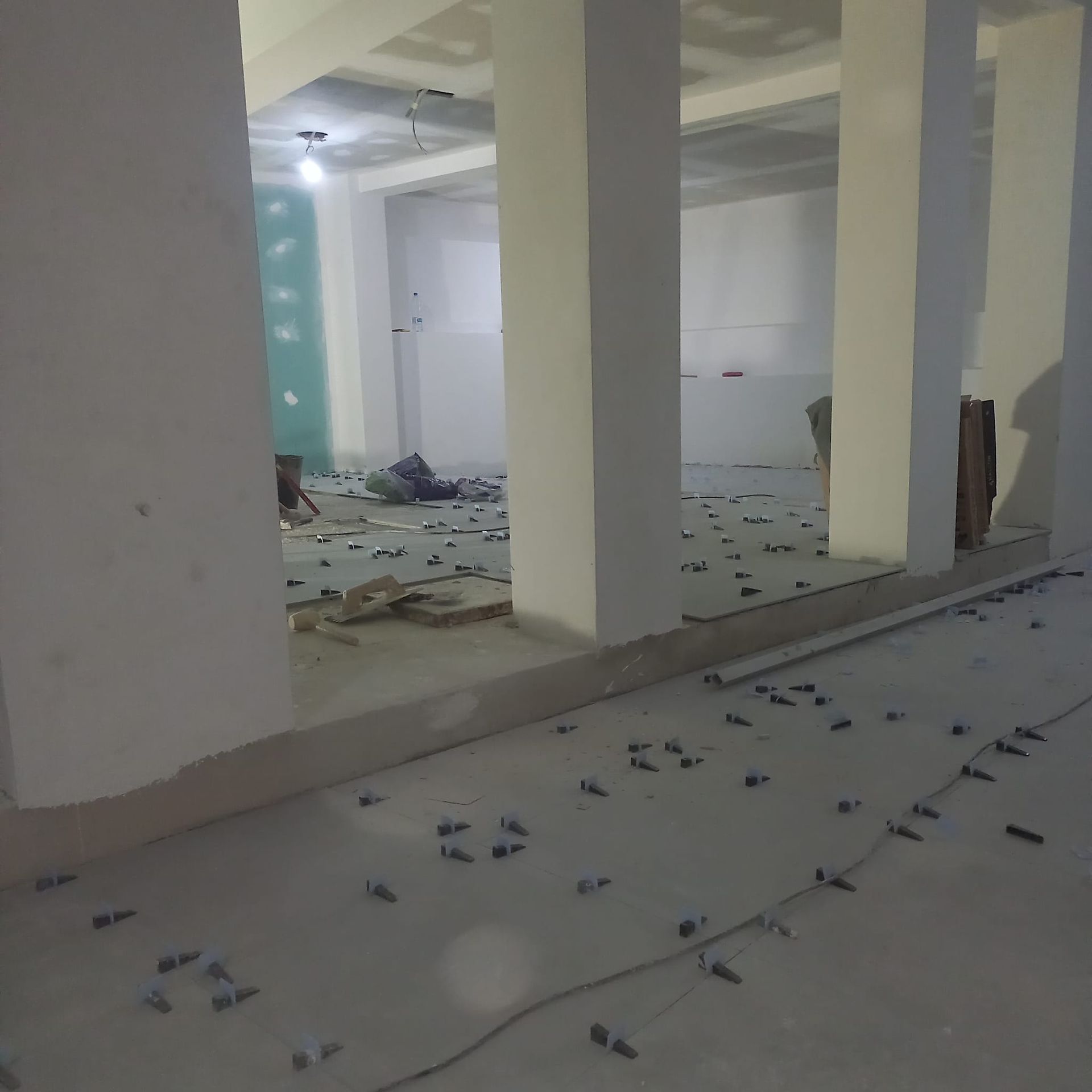 Una obra en construcción interior con pilares de hormigón y un suelo cubierto de pequeñas grapas de construcción oscuras.