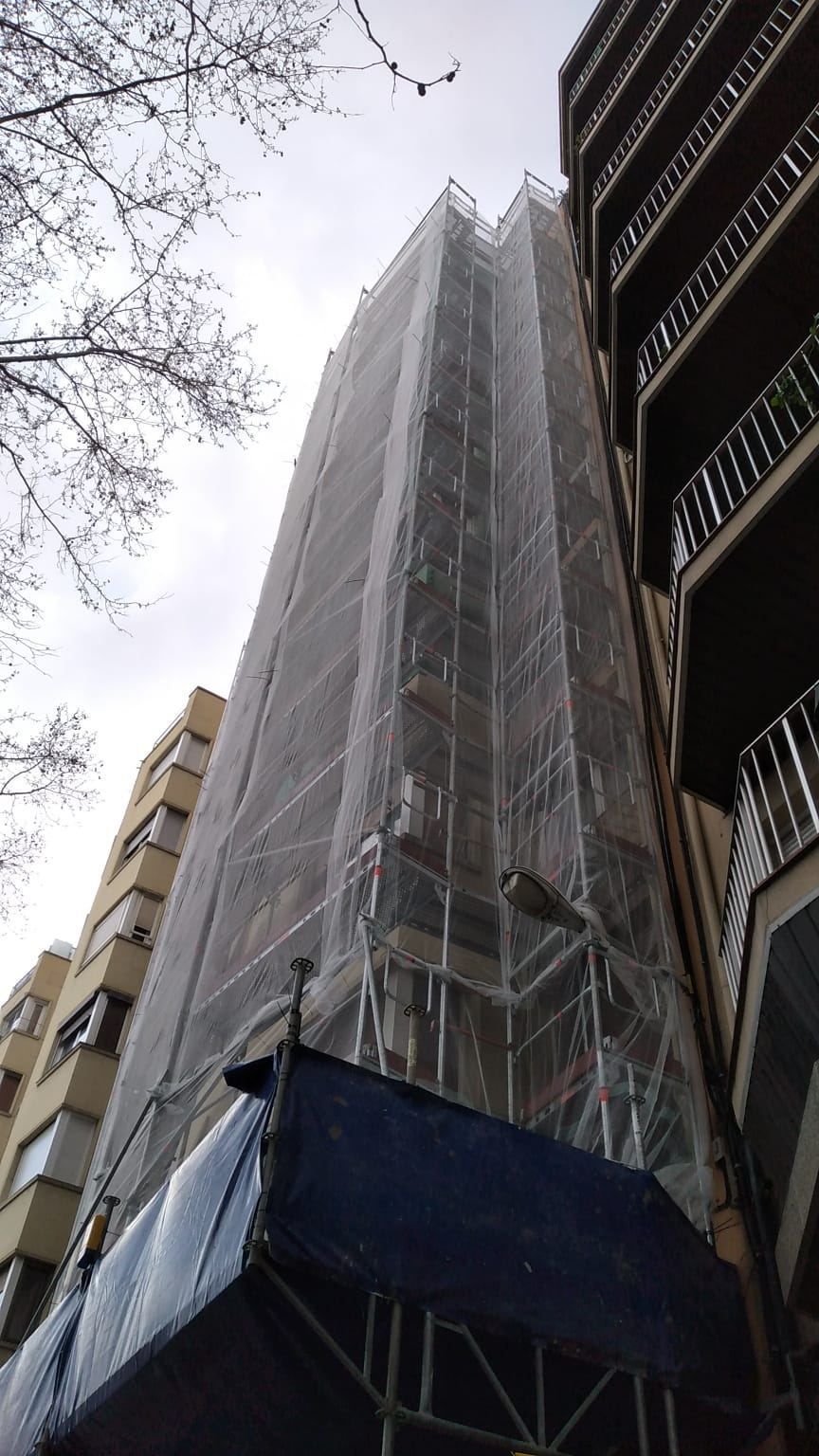 Edificio alto cubierto de andamios y redes de protección; construcción en progreso.