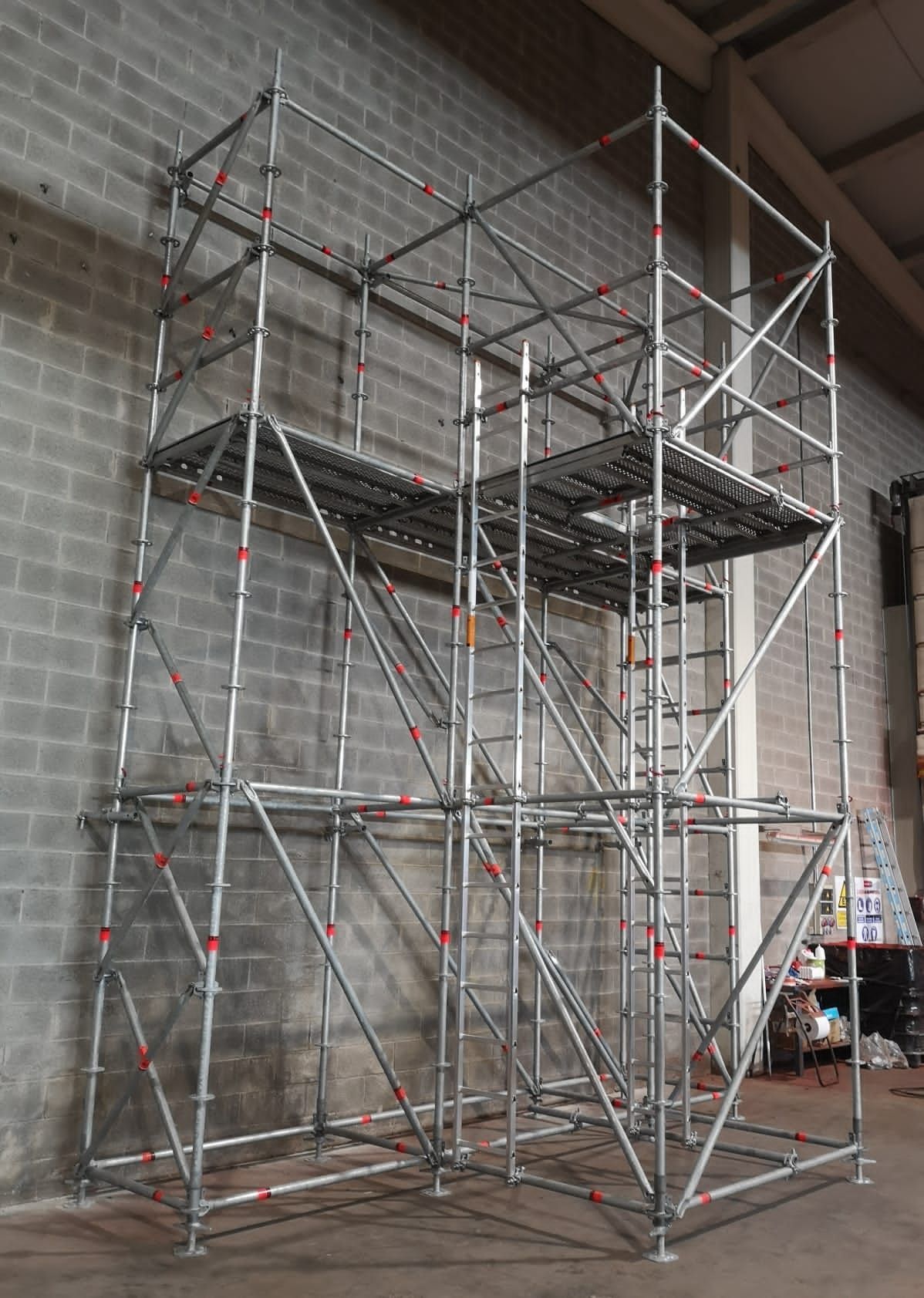 Estructura de andamio en entorno de almacén, compuesta por tubos metálicos con plataformas y arriostramientos diagonales.