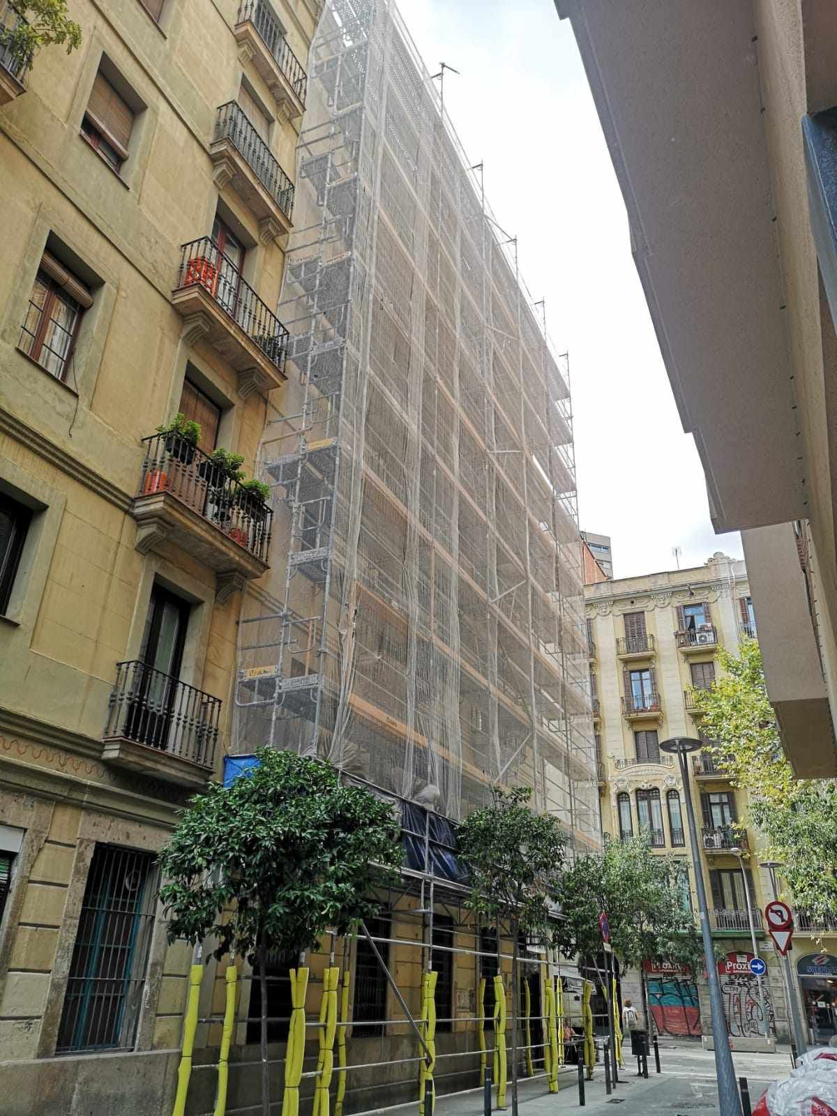 Edificio en construcción, cubierto de andamios y redes de seguridad, árboles en primer plano, Barcelona, ​​España.
