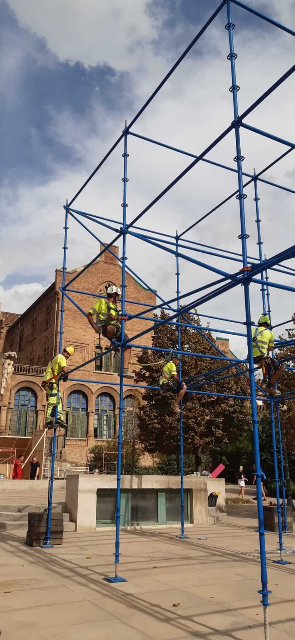 Obreros de la construcción en un andamio frente a un edificio de ladrillo. Cielo azul.