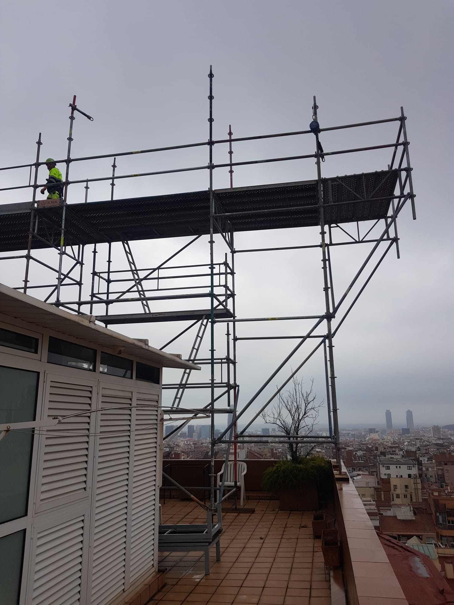 Andamio en la azotea con trabajador, con vistas a la ciudad en un día nublado.