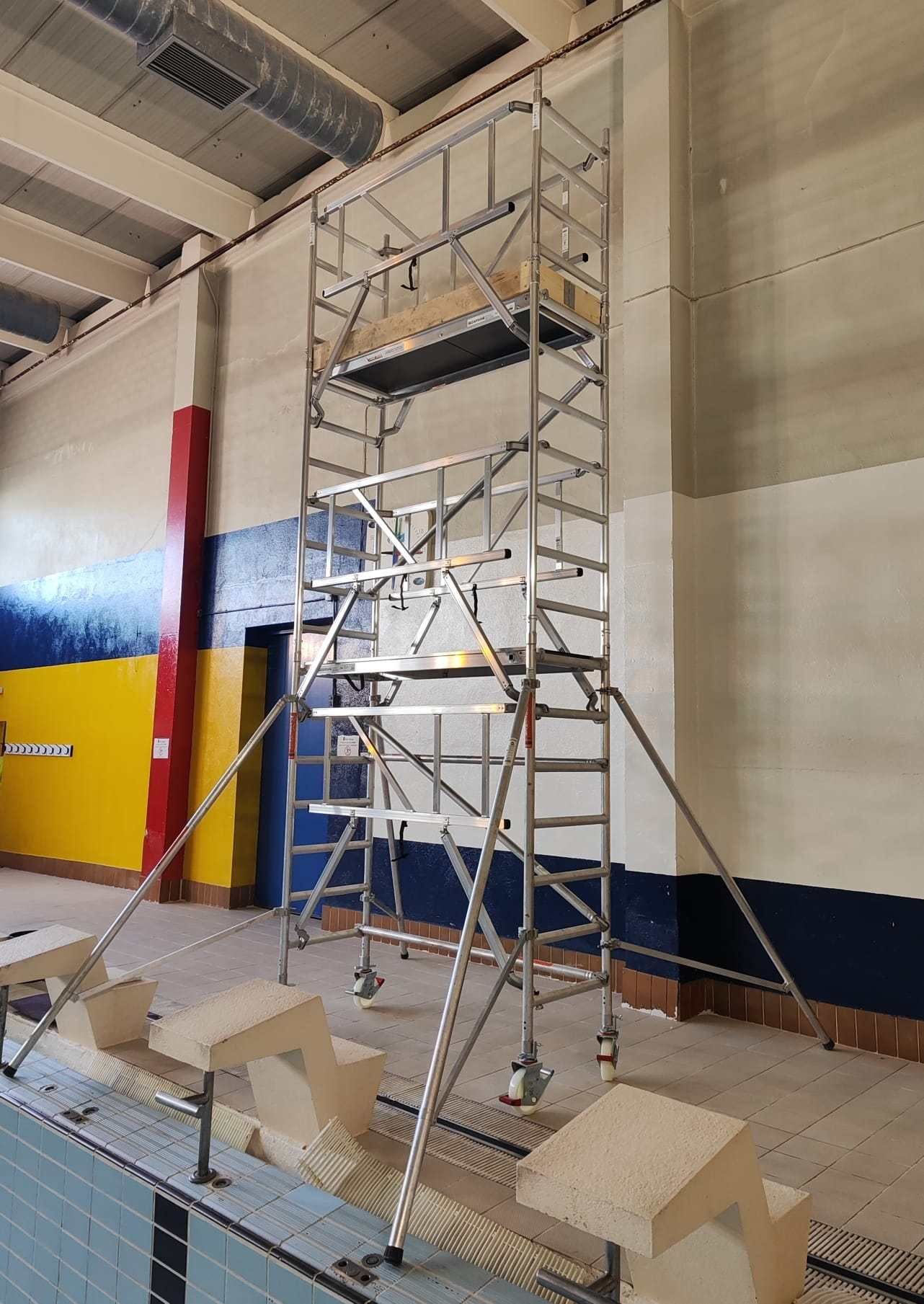 Andamio alto de aluminio en una piscina cubierta, colocado cerca de la pared.