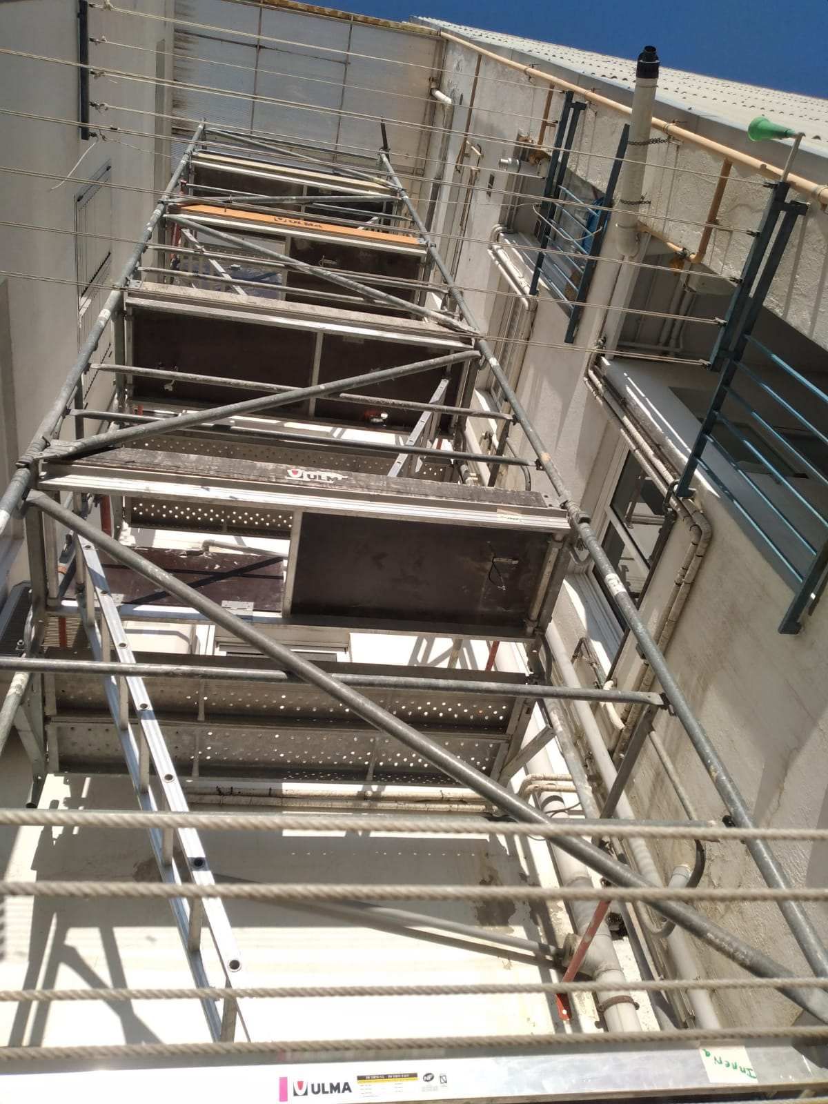 Andamio contra un edificio. Estructura metálica gris que se extiende hacia arriba con plataformas de madera.