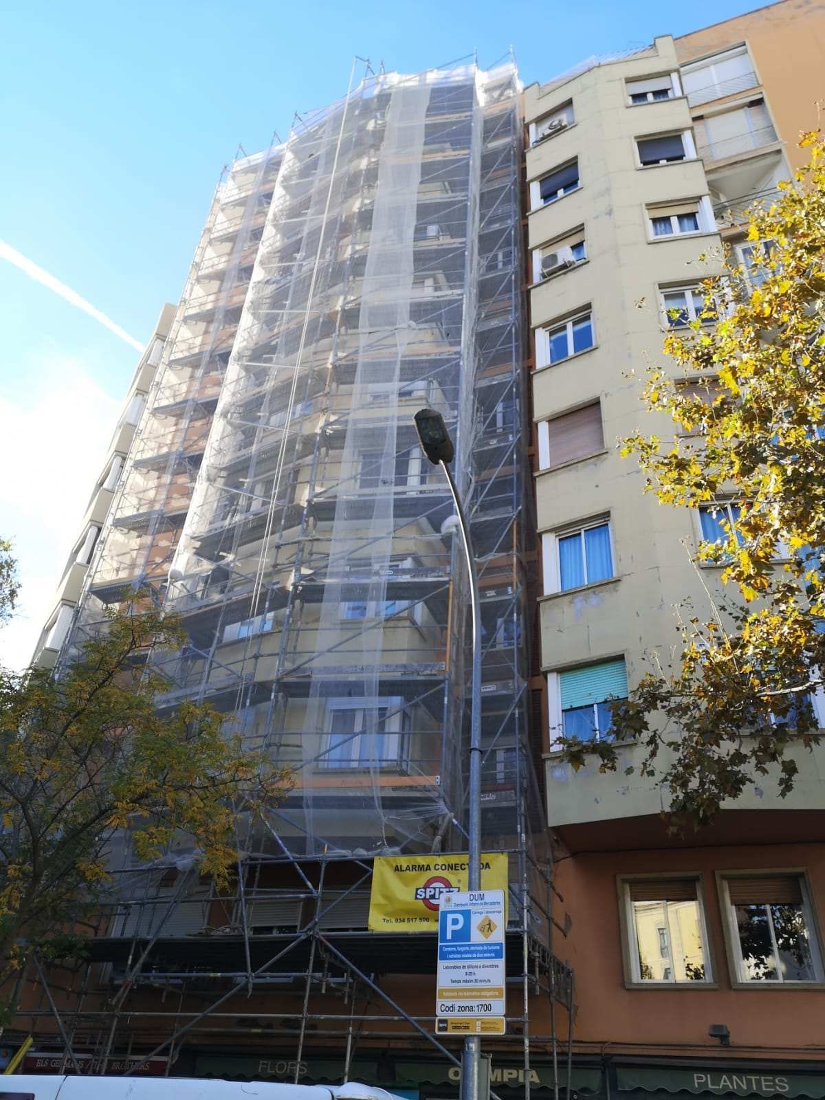 Edificio parcialmente cubierto con andamios y redes de seguridad, en proceso de renovación. Edificio adyacente visible.