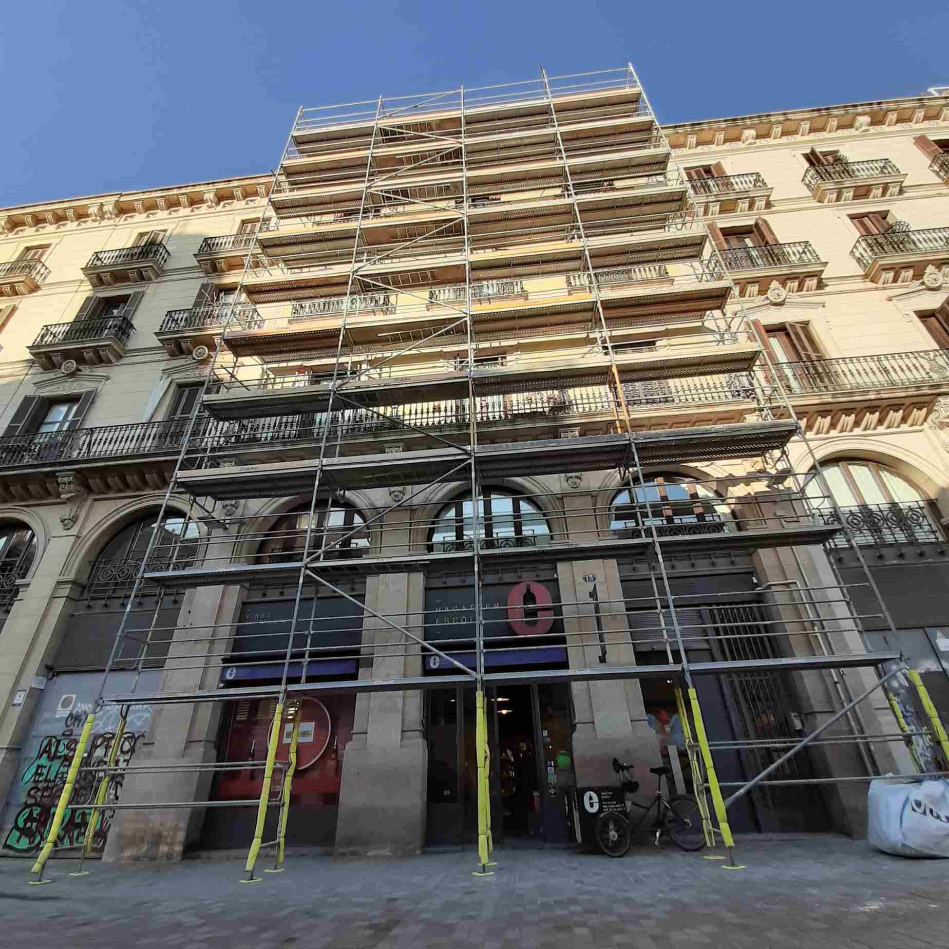 Fachada de edificio con andamios. Local comercial bajo arcos, a nivel de calle.