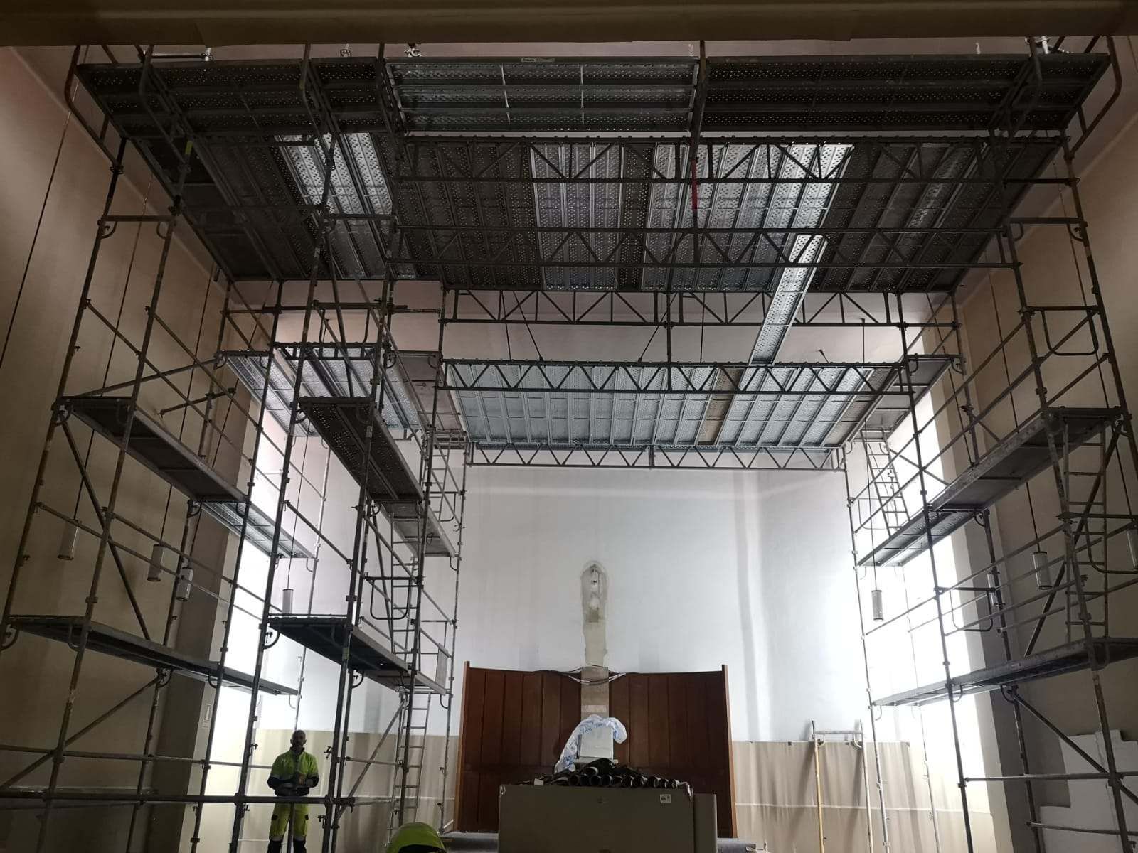 Andamios dentro de un edificio para trabajos de construcción en el techo. Dos trabajadores están presentes.