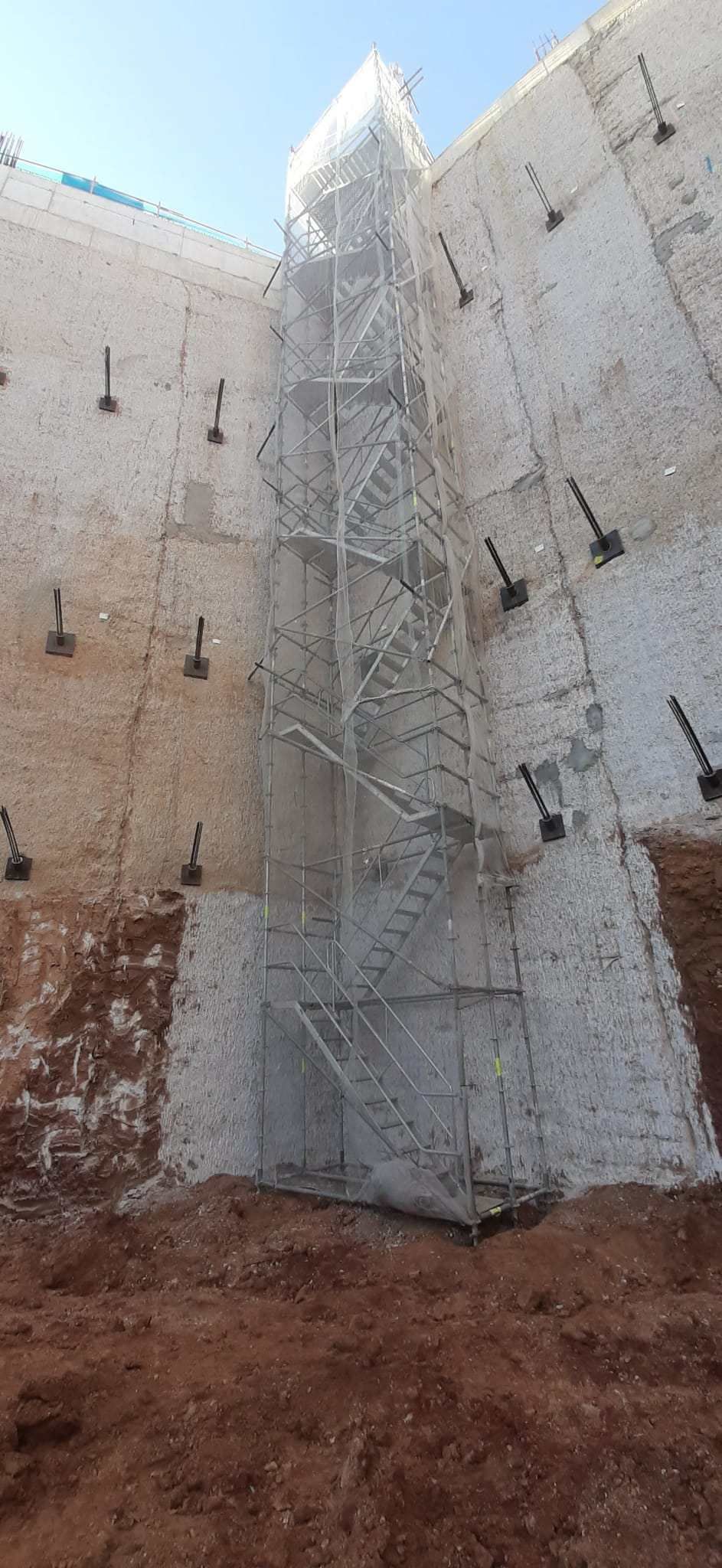 Muro de contención de hormigón en construcción. El muro se apoya en anclajes metálicos y una estructura de soporte central.