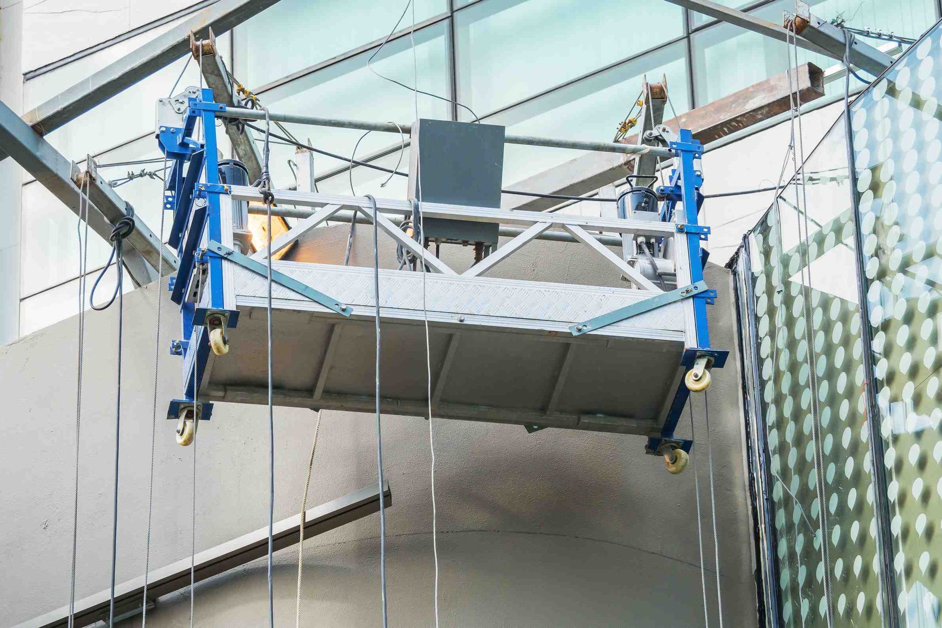 Plataforma suspendida de color azul y plata para limpieza de ventanas, colgada en el interior de un edificio.