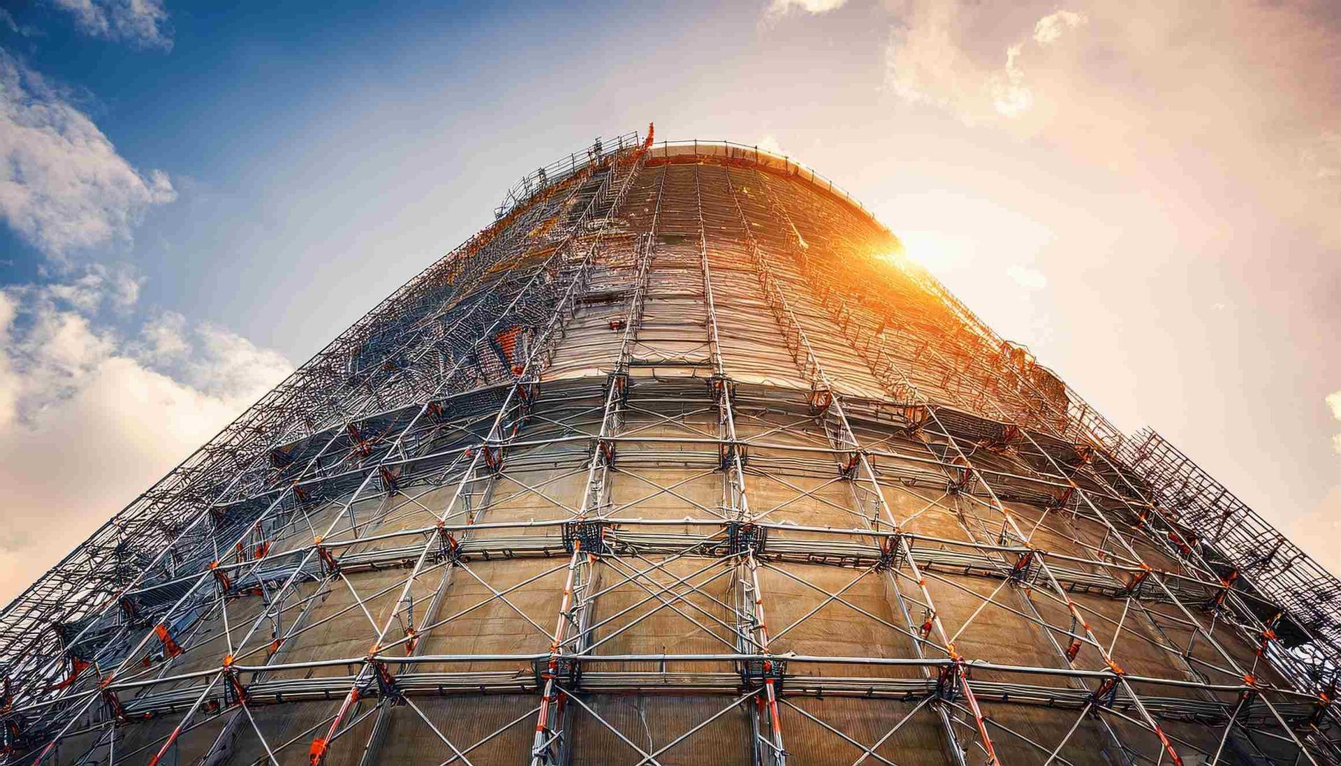 Una estructura alta y cilíndrica que se construye con andamios, frente a un cielo azul con un sol brillante.