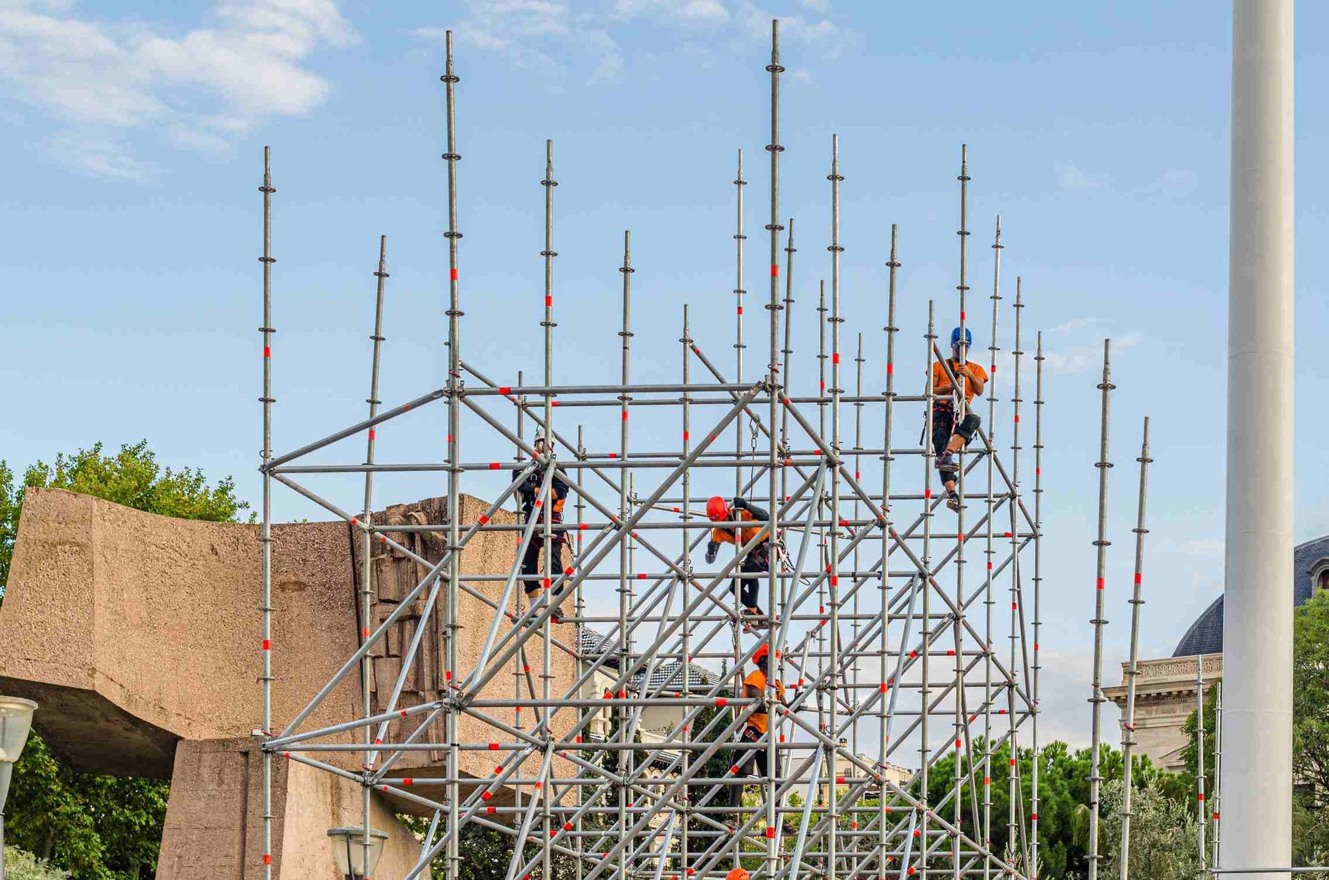 Obreros montan andamios alrededor de una gran escultura de piedra al aire libre, bajo un cielo nublado.