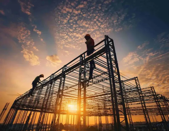 Trabajadores de la construcción en un edificio con estructura de acero al atardecer.