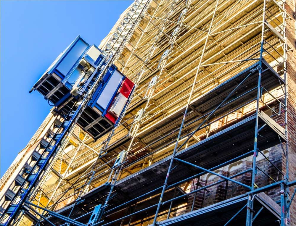 Andamio y ascensor en un edificio de ladrillo, bajo un cielo azul, durante la renovación.